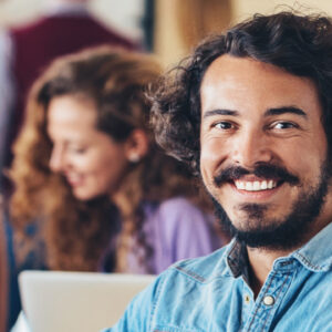A smiling man sits at the end of a boardroom table of professionals in a meeting