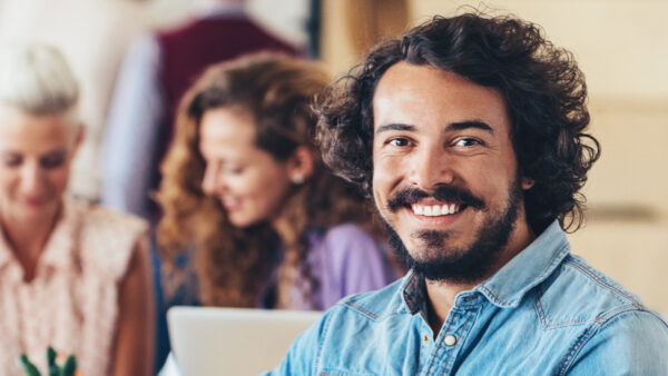 A smiling man sits at the end of a boardroom table of professionals in a meeting